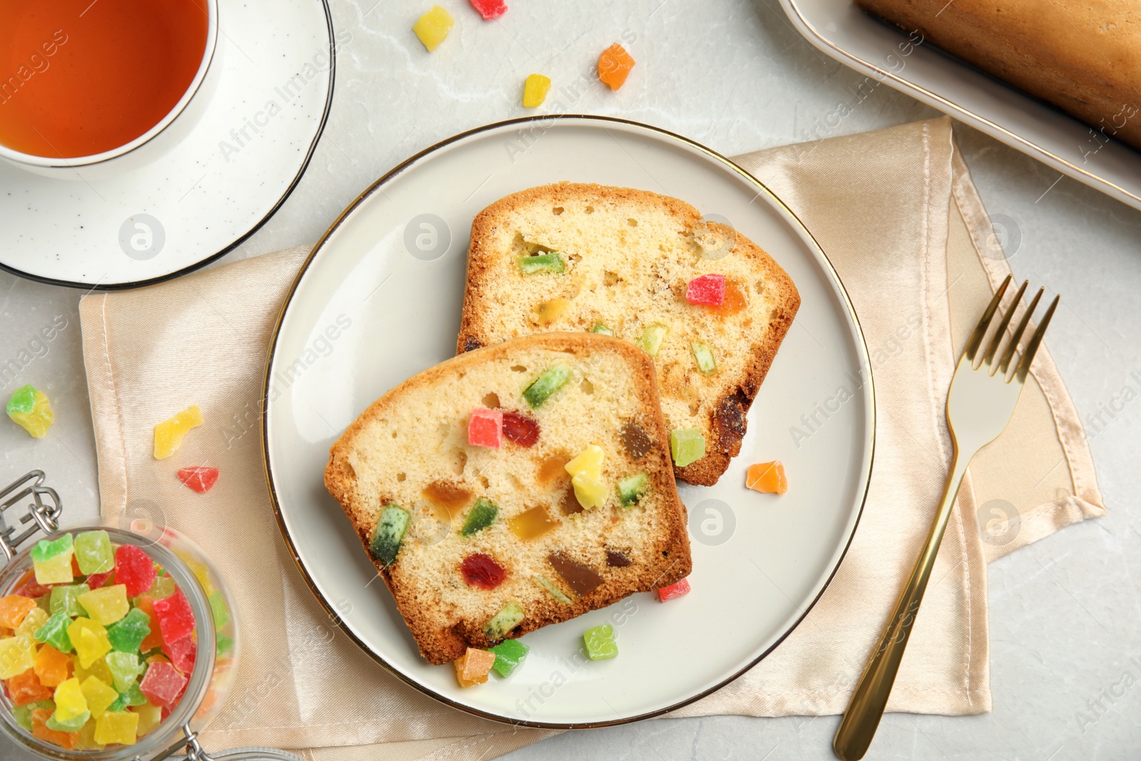 Photo of Delicious cake with candied fruits and tea on light table, flat lay