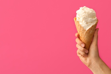 Woman holding waffle cone with delicious ice cream on pink background, closeup. Space for text