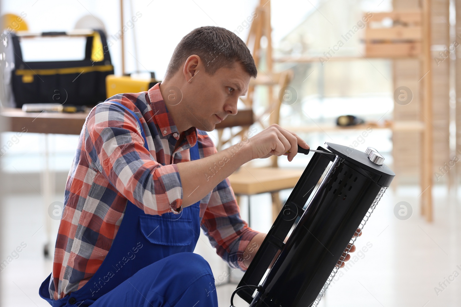 Photo of Professional technician repairing electric halogen heater with screwdriver indoors