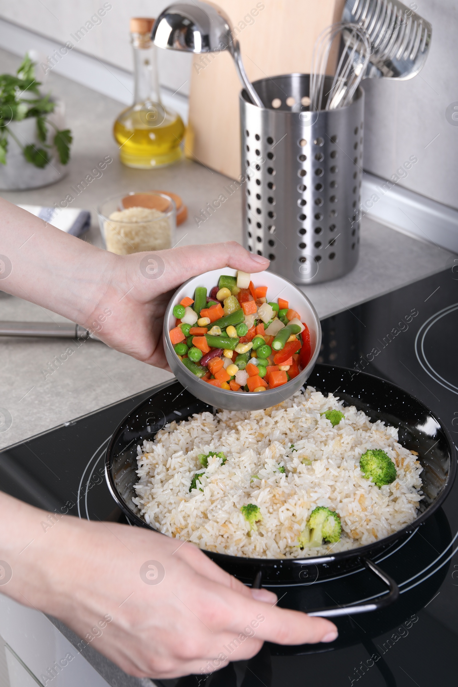 Photo of Woman cooking tasty rice with vegetables on induction stove, closeup