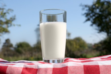 Photo of Glass of fresh milk on checkered blanket outdoors