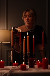 Beautiful young woman lightning up candle at table indoors