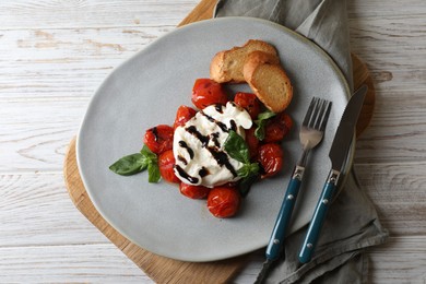 Delicious burrata cheese served with tomatoes, croutons and basil sauce on white wooden table, top view