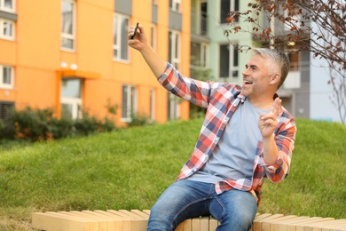 Photo of Handsome mature man taking selfie in park. Space for text