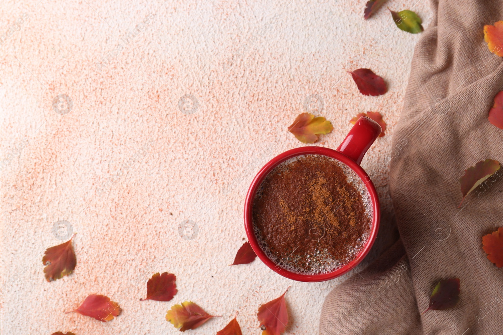 Photo of Cup of hot drink, leaves and soft knitted fabric on beige textured table, flat lay with space for text. Cozy autumn atmosphere