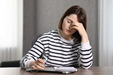 Photo of Overwhelmed woman sitting at wooden table with laptop and stationery indoors