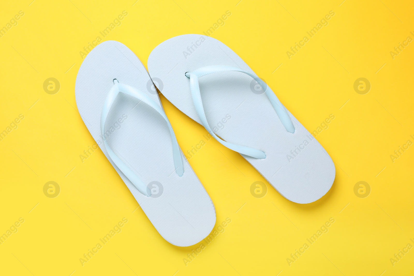Photo of Stylish white flip flops on yellow background, top view