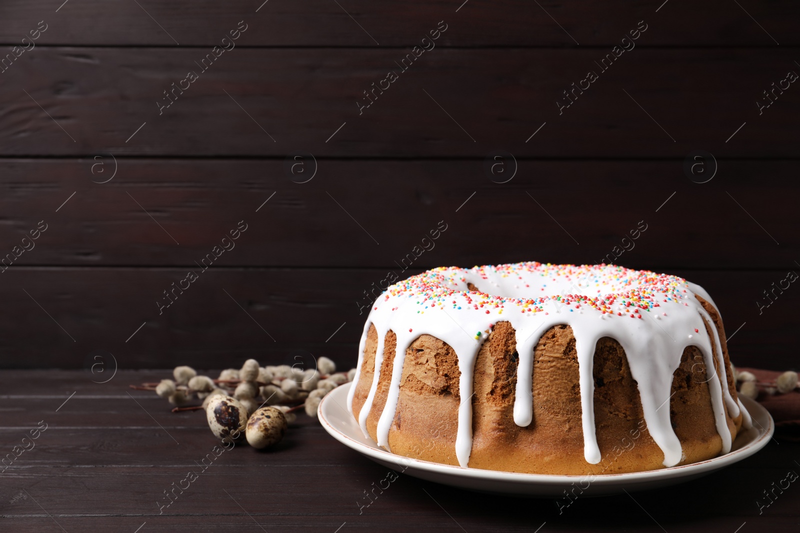 Photo of Glazed Easter cake with sprinkles, quail eggs and willow branches on wooden table. Space for text