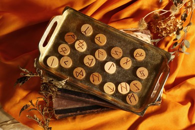 Photo of Tray with wooden runes, dried plants and old books on orange fabric, flat lay