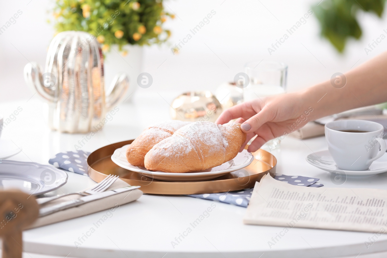 Photo of Woman taking fresh croissant from plate on table