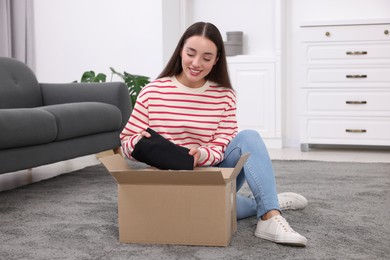 Happy young woman taking black jeans out of box at home. Online shopping