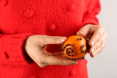 Photo of Woman decorating fresh tangerine with cloves, closeup. Making Christmas pomander ball