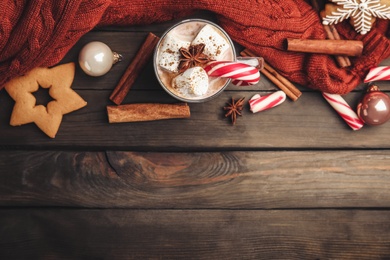 Photo of Flat lay composition with glass cup of tasty cocoa and Christmas candy cane on wooden table. Space for text