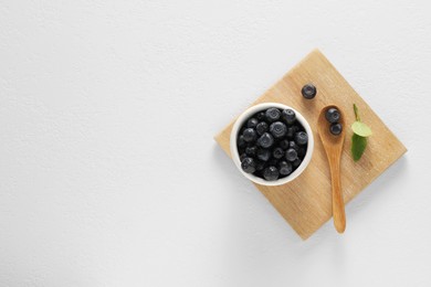 Photo of Ripe bilberries and leaves on white table, top view. Space for text