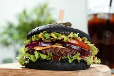 Photo of Board with juicy black burger, closeup view