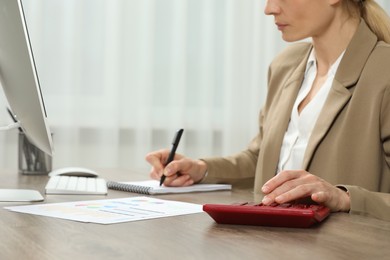 Professional accountant using calculator at wooden desk in office, closeup