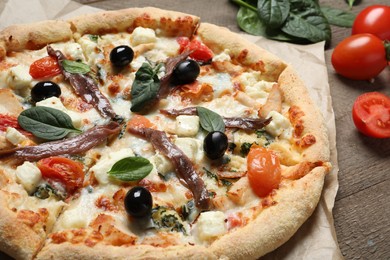Photo of Tasty pizza with anchovies and ingredients on wooden table, closeup