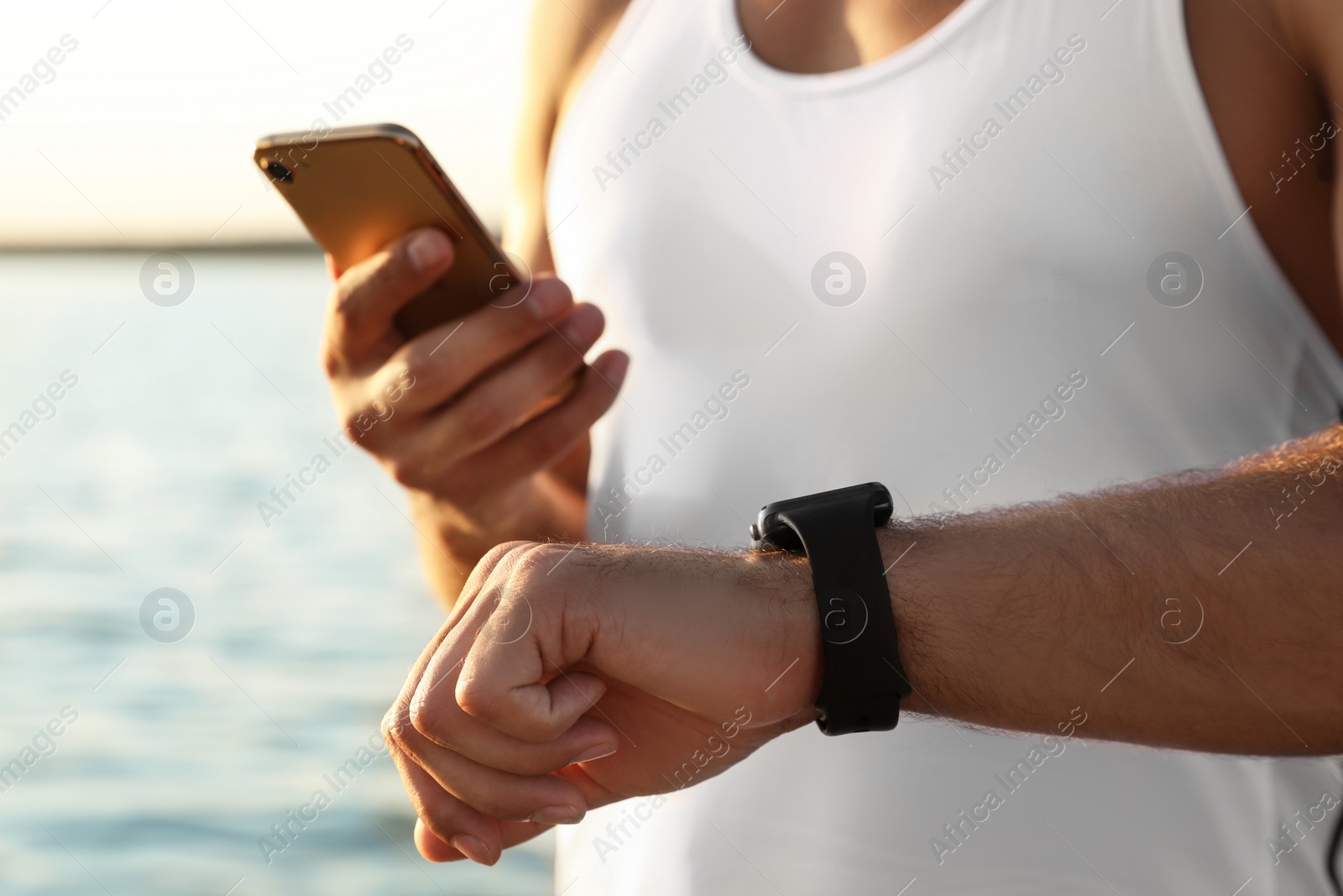 Photo of Man with fitness tracker and smartphone checking results after training near river, closeup
