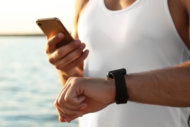 Photo of Man with fitness tracker and smartphone checking results after training near river, closeup