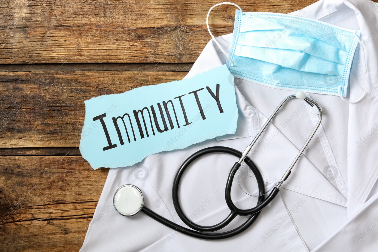 Photo of Paper piece with word Immunity and medical items on wooden table, flat lay