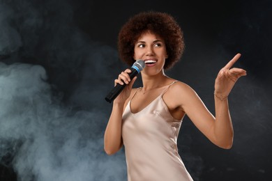 Photo of Curly young woman with microphone singing in smoke on black background