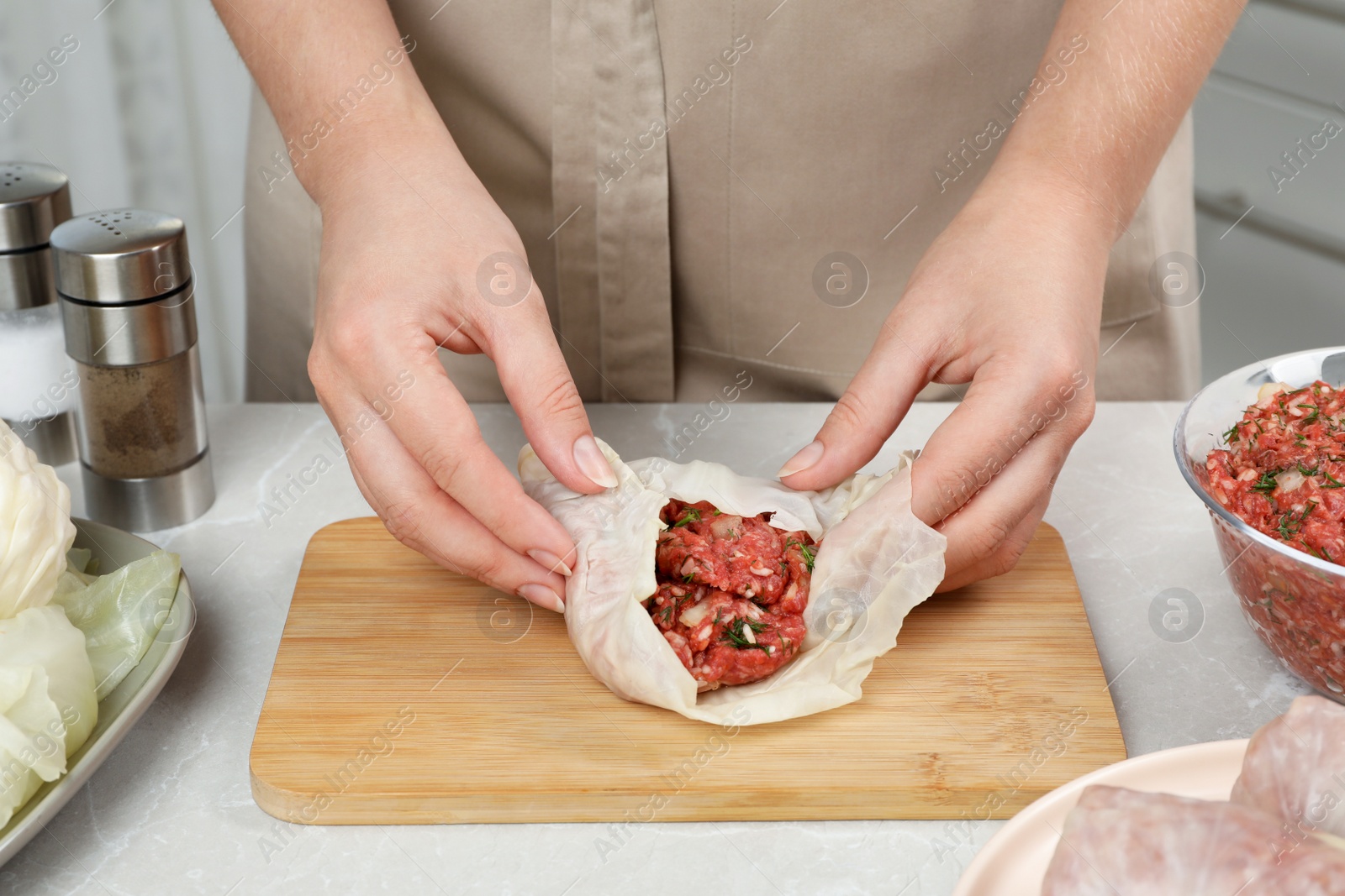 Photo of Woman preparing stuffed cabbage rolls at light grey table, closeup