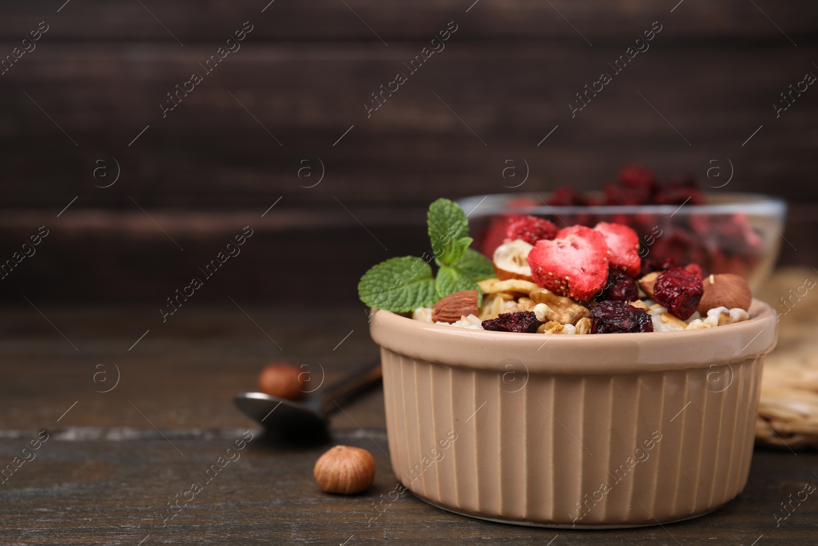 Photo of Oatmeal with freeze dried fruits, nuts and mint on wooden table, closeup. Space for text