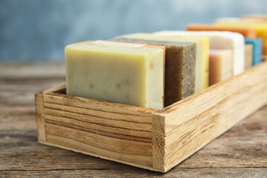 Photo of Many different handmade soap bars in wooden box on table, closeup