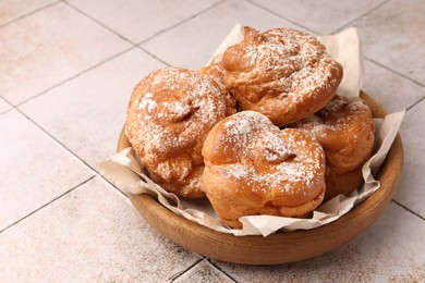 Photo of Delicious profiteroles with powdered sugar on white tiled table, space for text