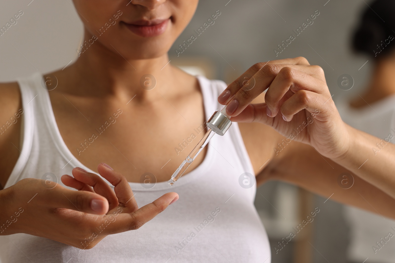 Photo of Woman applying serum onto her finger indoors, closeup