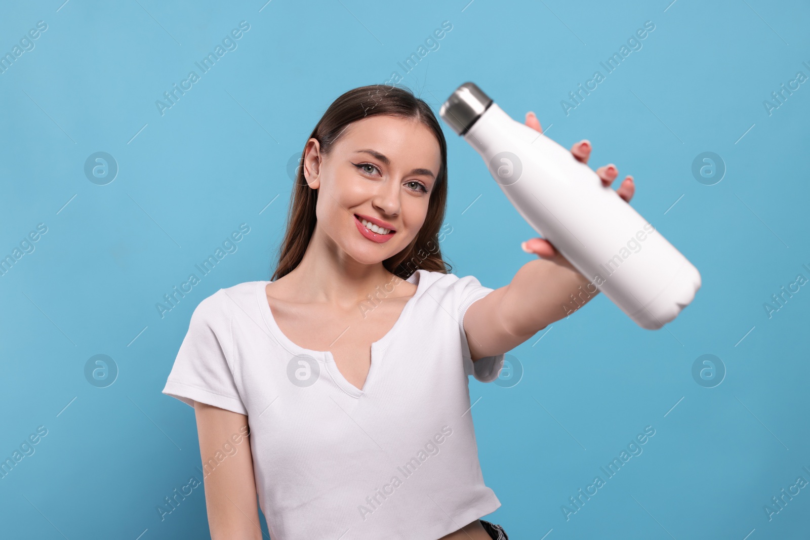 Photo of Beautiful young woman with thermos bottle on light blue background