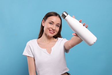 Beautiful young woman with thermos bottle on light blue background