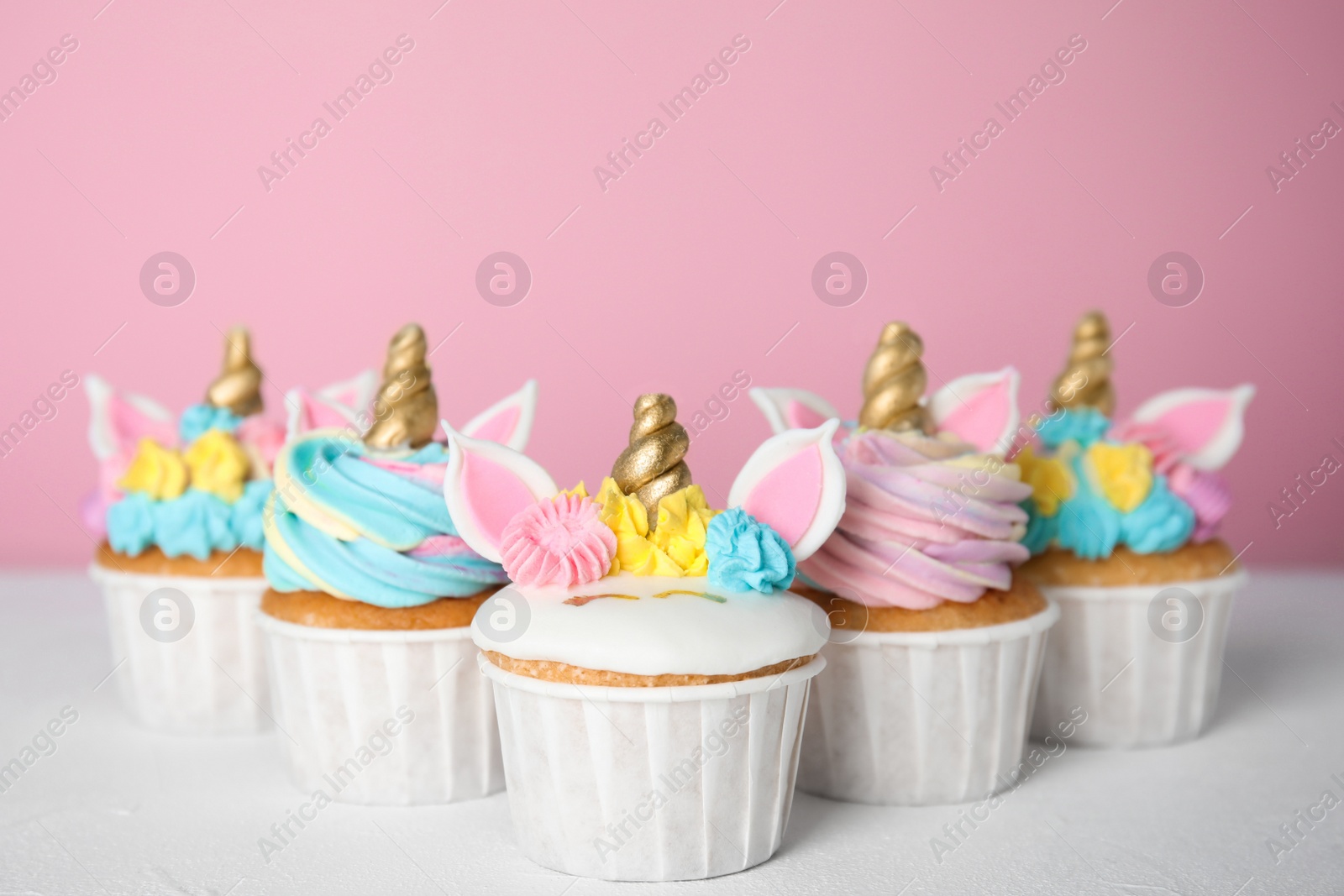 Photo of Many cute sweet unicorn cupcakes on white table against pink background