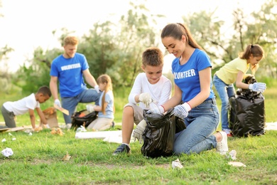 Photo of Little boy collecting trash with volunteer in park