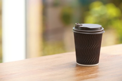 Photo of Cardboard cup of coffee on table against blurred background. Space for text