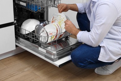 Photo of Man loading dishwasher with dirty plates indoors, closeup