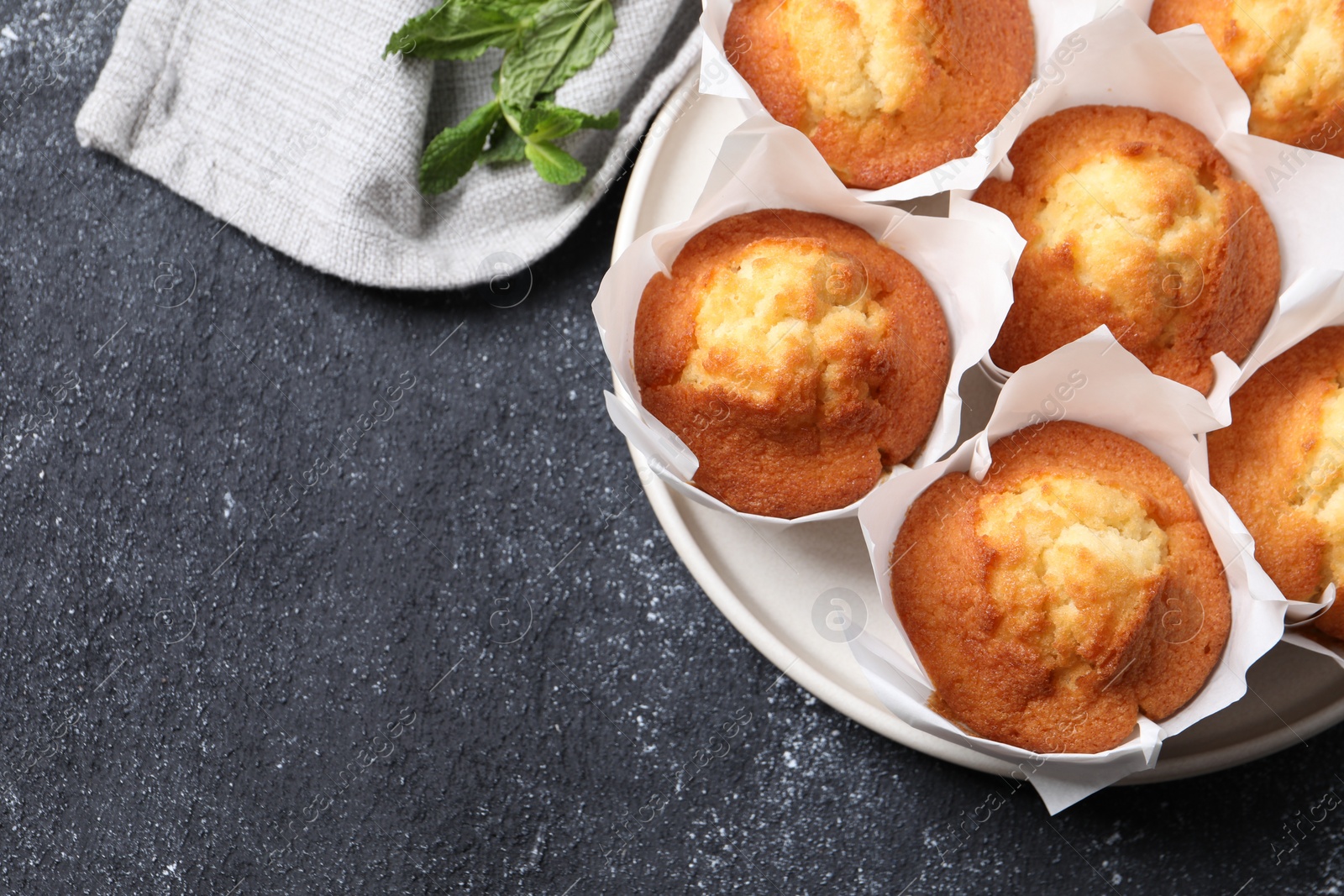 Photo of Delicious sweet muffins on black textured table, top view. Space for text