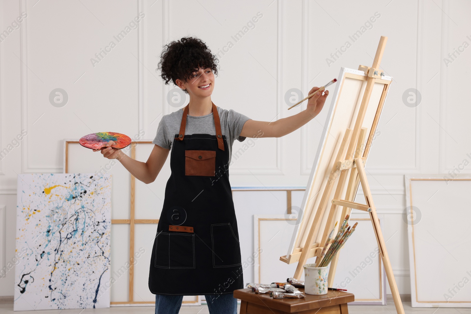 Photo of Young woman painting on easel with canvas in studio