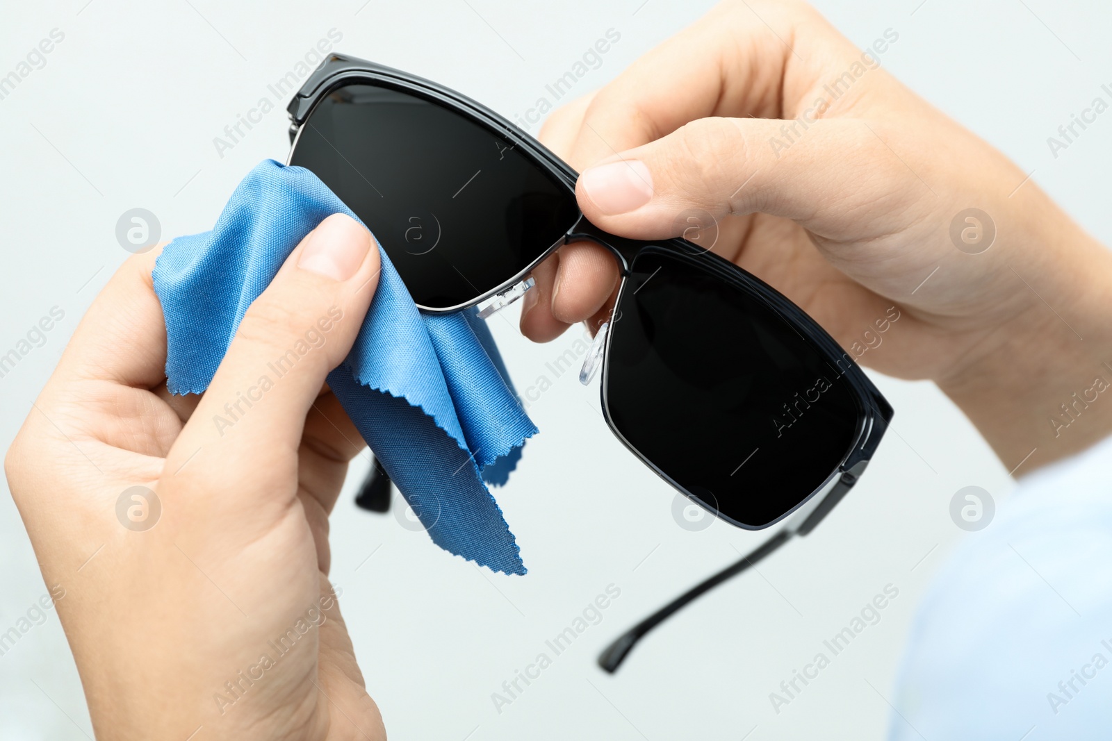 Photo of Woman wiping sunglasses with microfiber cleaning cloth on light background, closeup