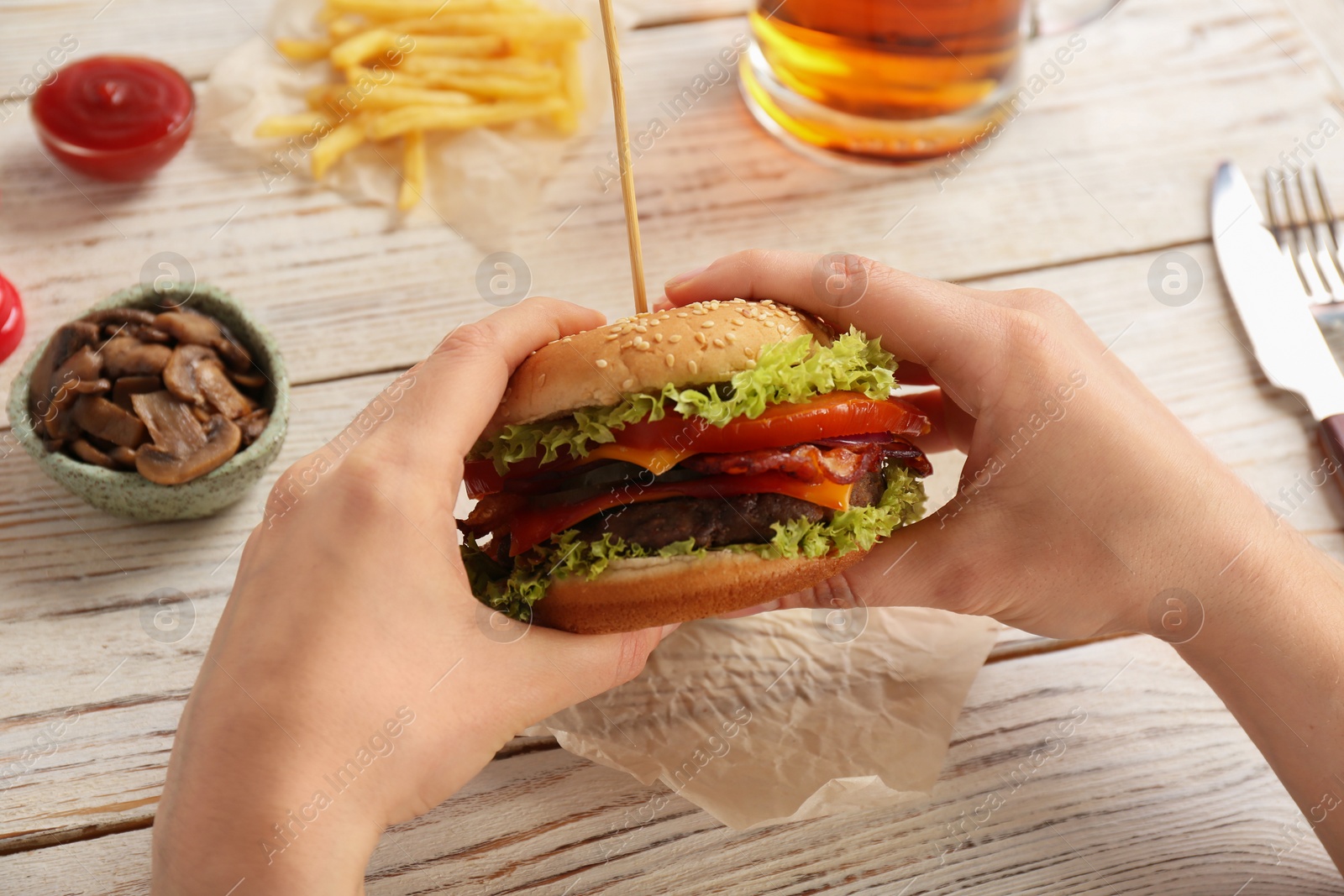 Photo of Woman holding tasty burger with bacon over wooden table, closeup