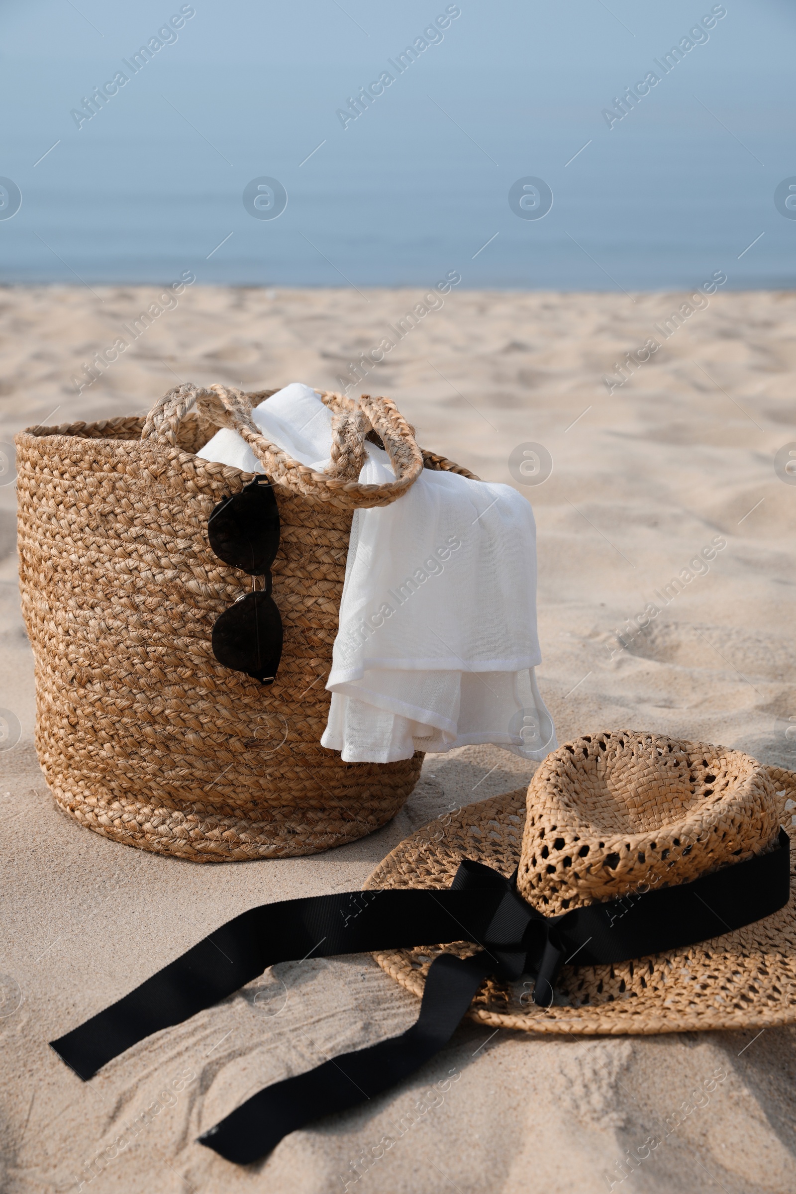 Photo of Beach bag, towel, sunglasses and hat on sandy seashore