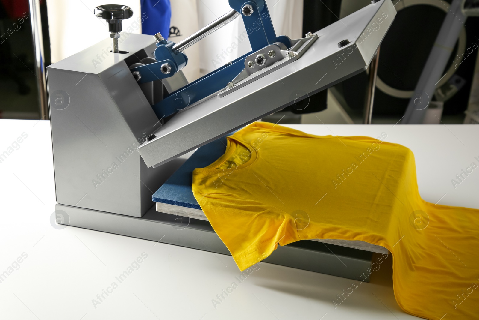 Photo of Printing logo. Heat press with yellow t-shirt on white table