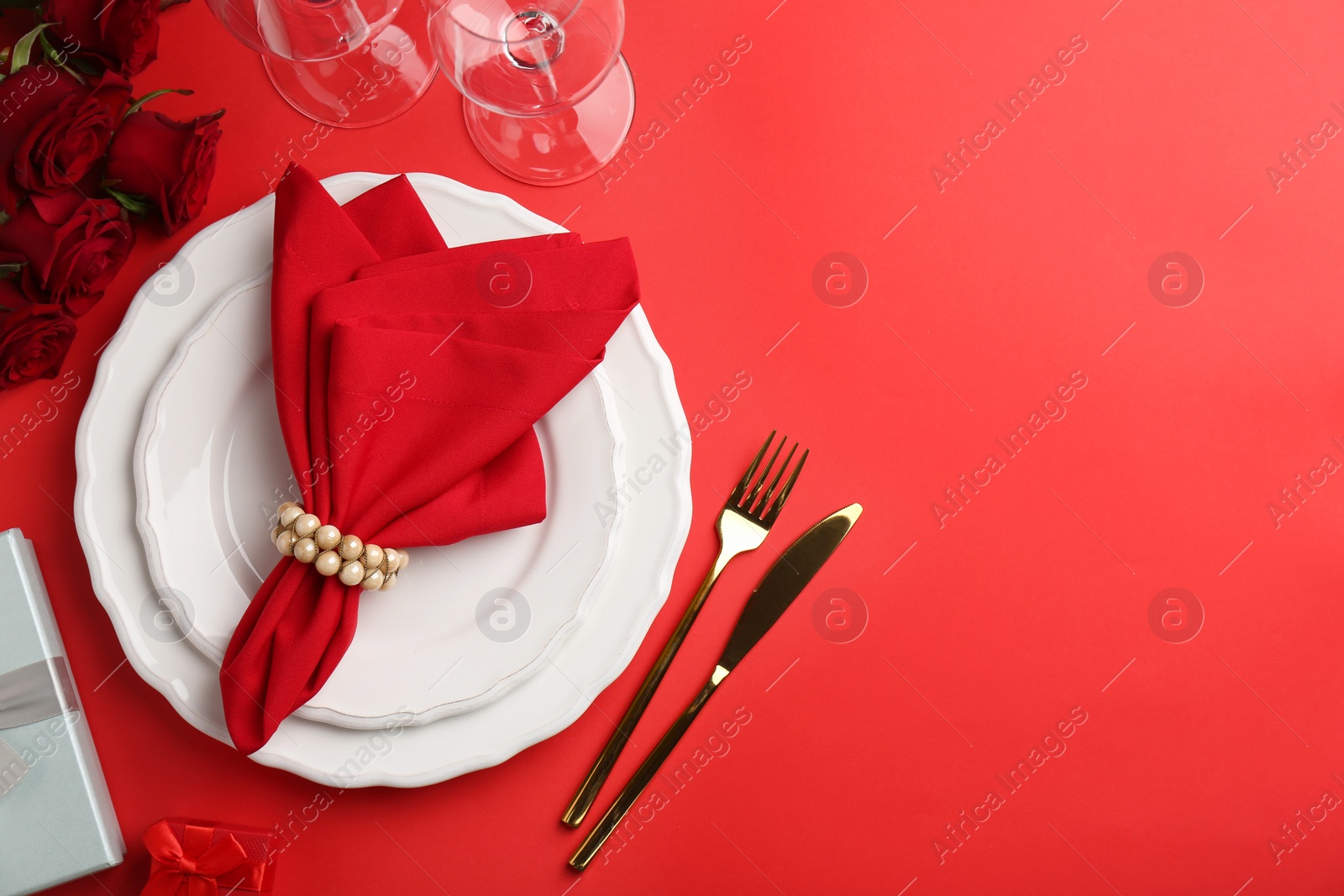 Photo of Place setting with gift boxes and bouquet of roses for romantic dinner on red table, flat lay. Space for text