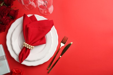 Photo of Place setting with gift boxes and bouquet of roses for romantic dinner on red table, flat lay. Space for text