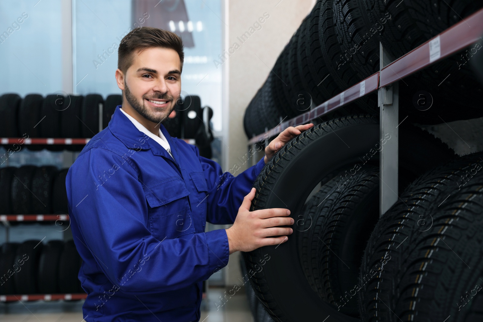 Photo of Male mechanic with car tire in auto store