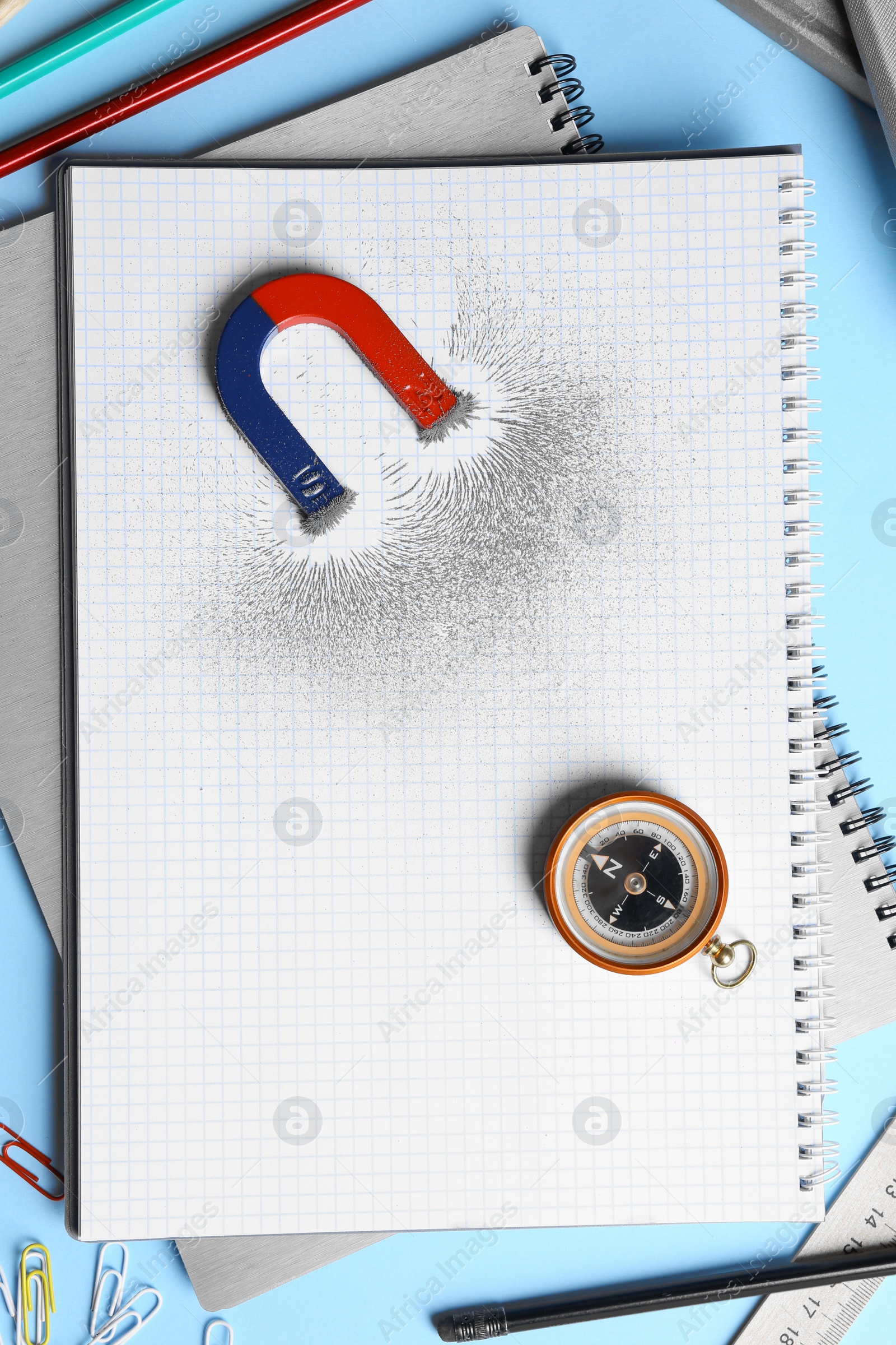 Photo of Notebook, stationery, compass and magnet with iron powder on blue background, flat lay