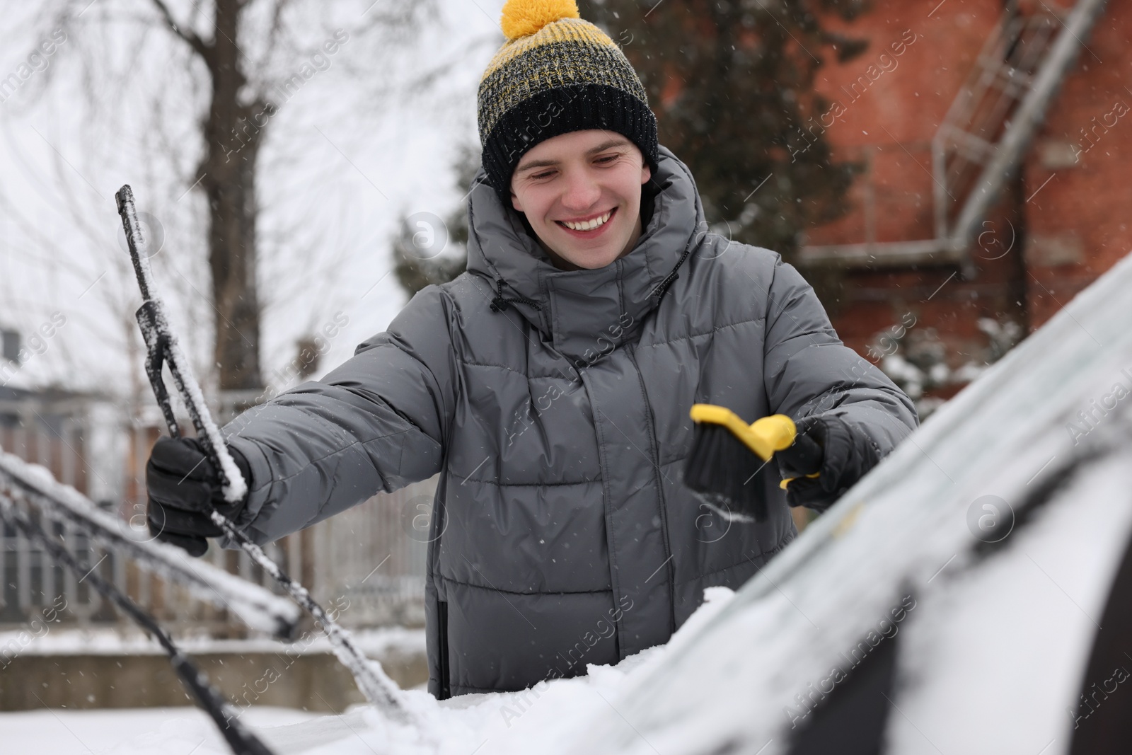 Photo of Man cleaning snow from car with brush outdoors