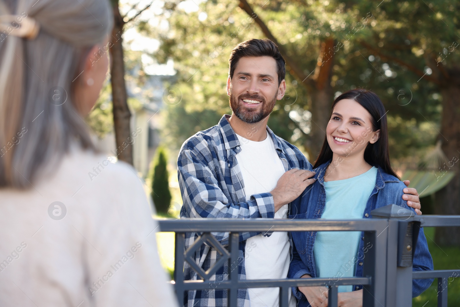 Photo of Friendly relationship with neighbours. Happy young couple and senior woman near fence outdoors