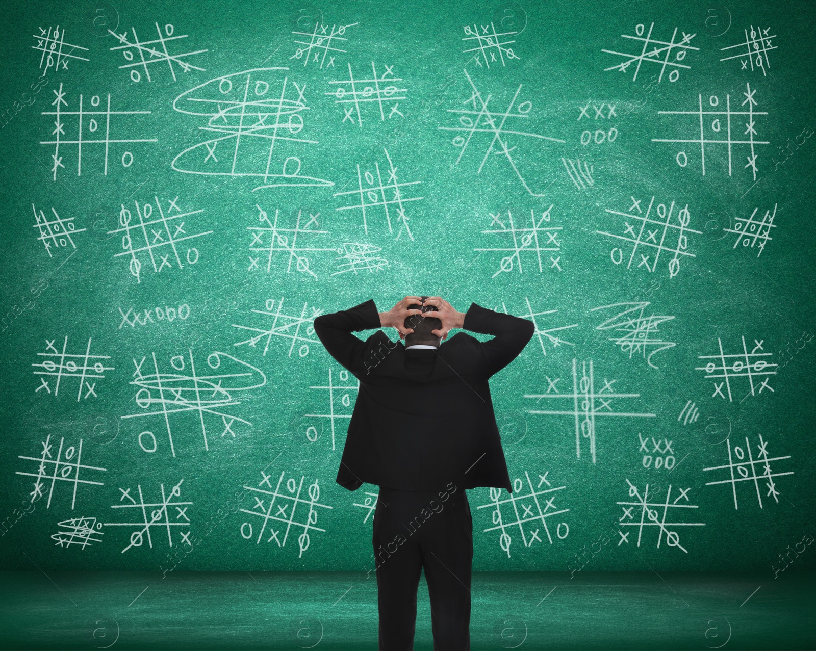 Image of Young businessman near green chalkboard with drawn tic tac toe game, back view