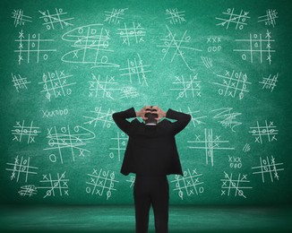 Young businessman near green chalkboard with drawn tic tac toe game, back view
